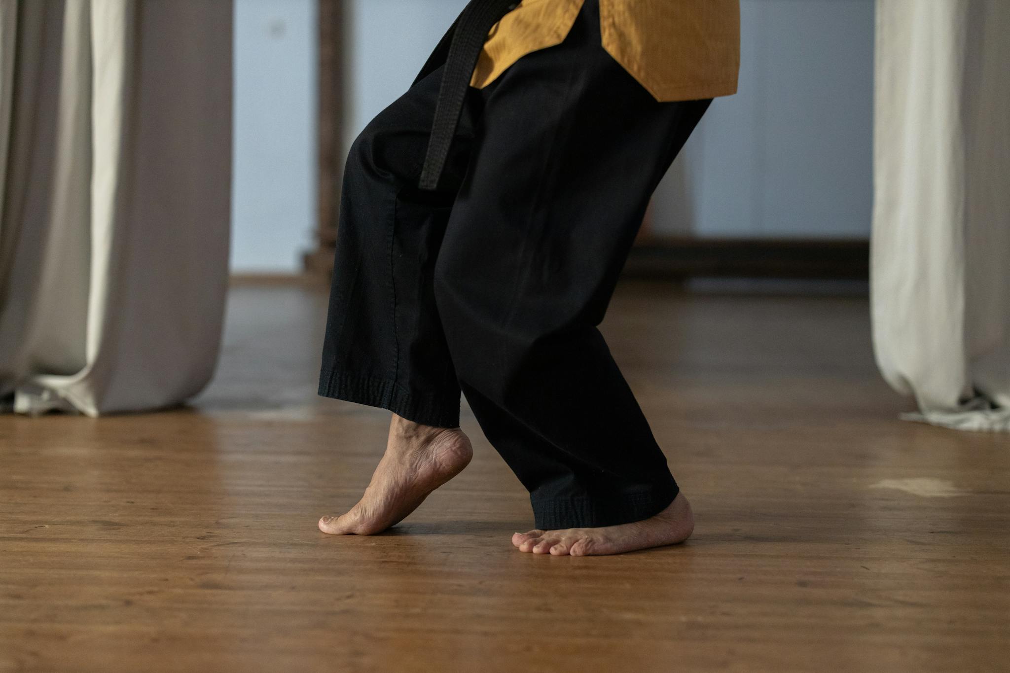 Person practicing martial arts barefoot on a wooden floor indoors.